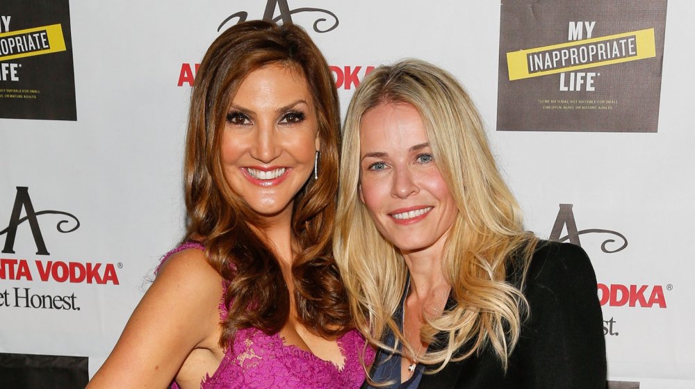 Heather McDonald in a purple, lace dress, and Chelsea Handler in a black outfit, smiling at a book party event in 2013