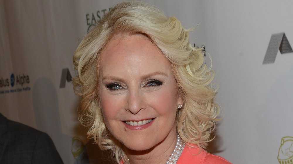 Cindy McCain smiling in a salmon-colored outfit and pearl necklace