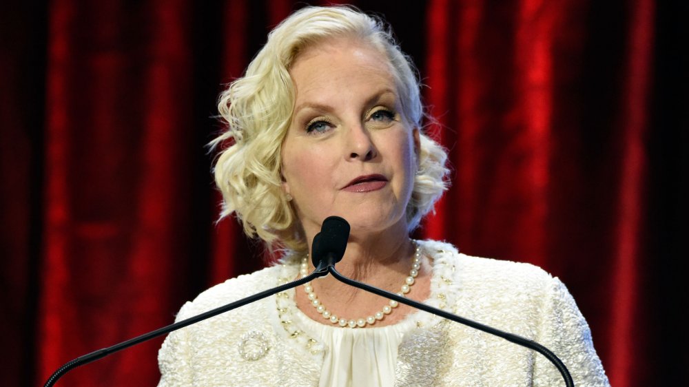 Cindy McCain in a white dress and pearls, speaking at an event