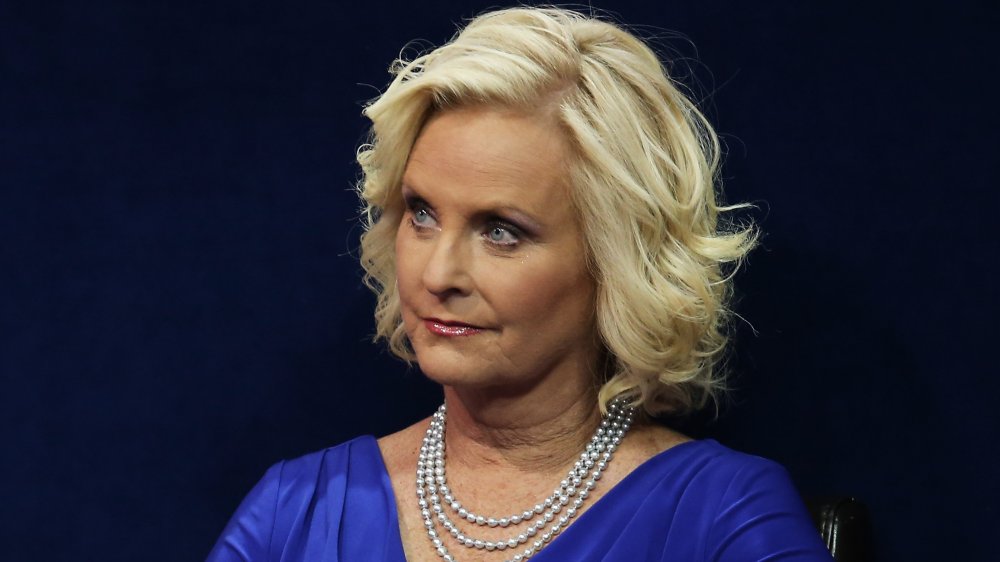 Cindy McCain in a blue dress and pearls, looking off to the side with a neutral expression