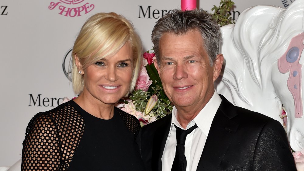 Yolanda Hadid in a black lace dress, David Foster in a black suit with loose black tie, smiling together at an event