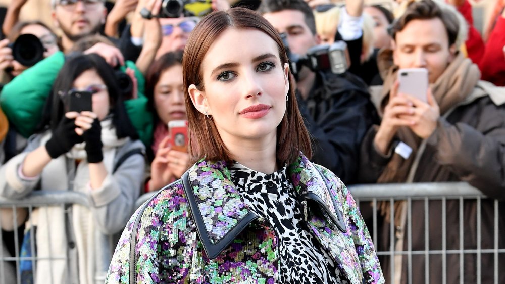 Emma Roberts being photographed by fans at an event, posing in colorfully printed clothes