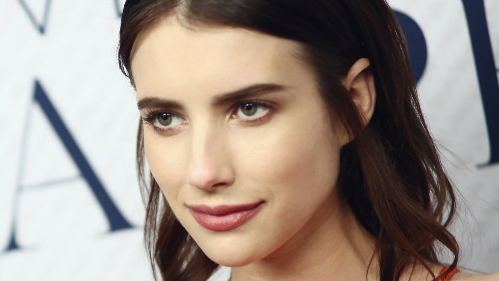 Emma Roberts posing on the red carpet, looking off to the side with a smirk