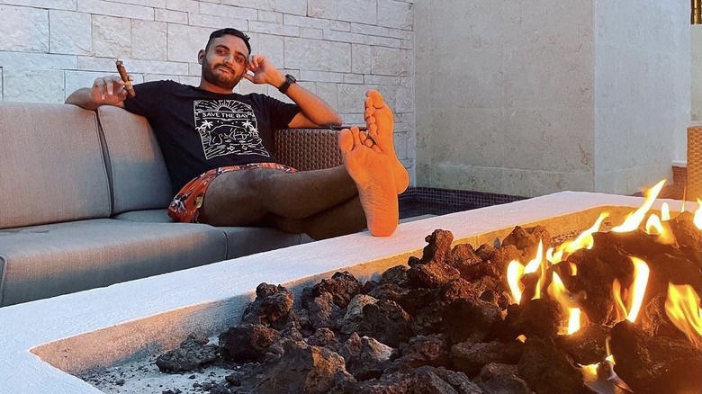 Shaan Patel relaxing by a fire, smoking a cigar