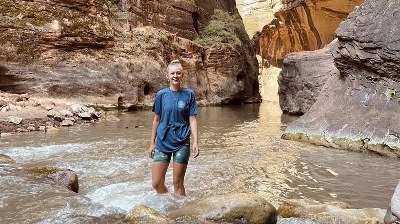 Gabby Petito smiling, wading in water among mountains