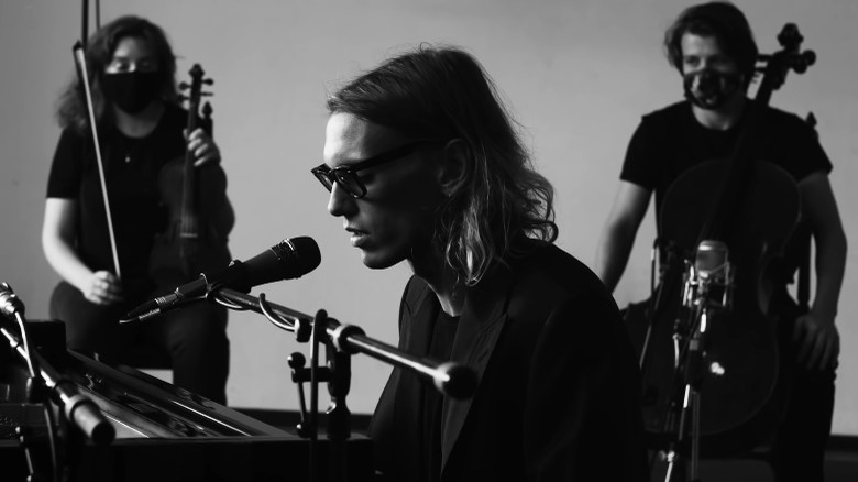 Jamie Campbell Bower at a piano, two musicians behind him