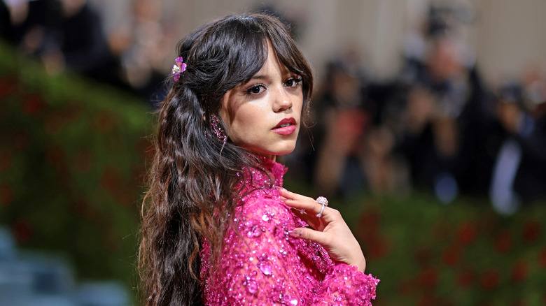 Jenna Ortega posing while looking over her shoulder in an all-pink outfit