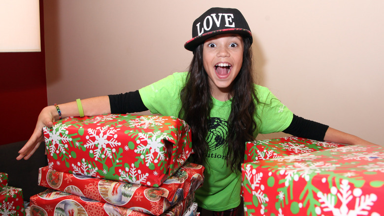 A young Jenna Ortega holding big Christmas presents