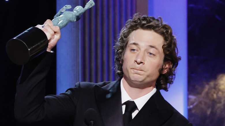 Jeremy Allen White on stage, holding trophy in air