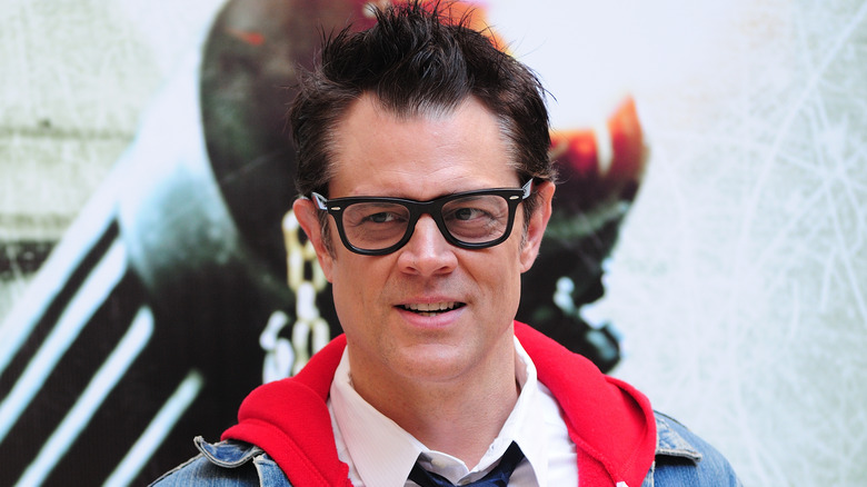 Johnny Knoxville in a red hoodie and tie