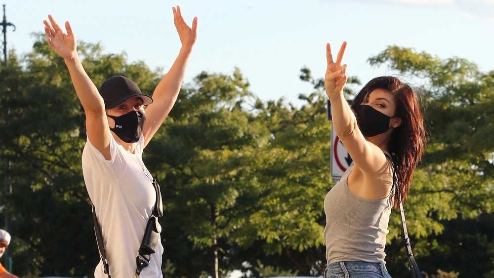 Kaley Cuoco and Briana Cuoco wearing masks outside with their hands in the air.
