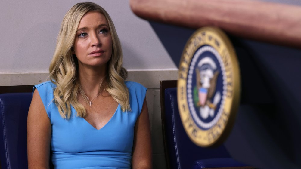 Kayleigh McEnany in a light blue dress, sitting while looking up at the White House press room podium