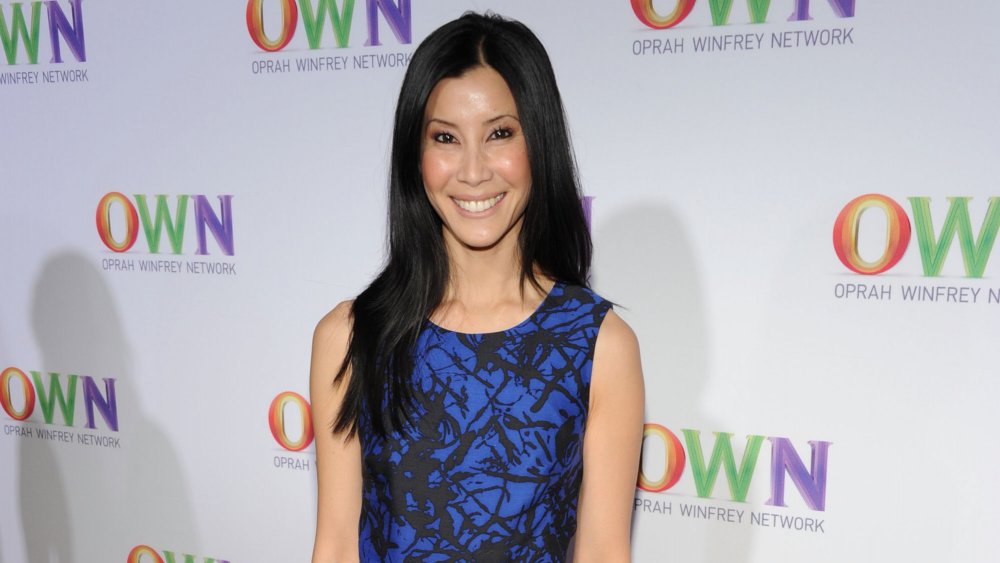 Lisa Ling in a blue and black dress in front of OWN wall