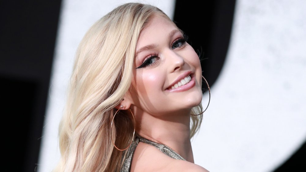 Loren Gray with blonde hair, wearing a silver dress, smiling and looking over her shoulder