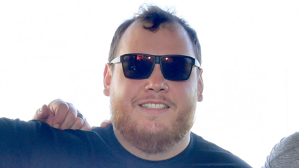 Luke Combs in a black t-shirt and sunglasses, smiling