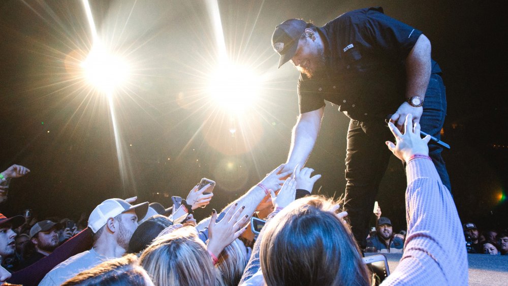 Luke Combs on stage, smiling and giving his fans high fives