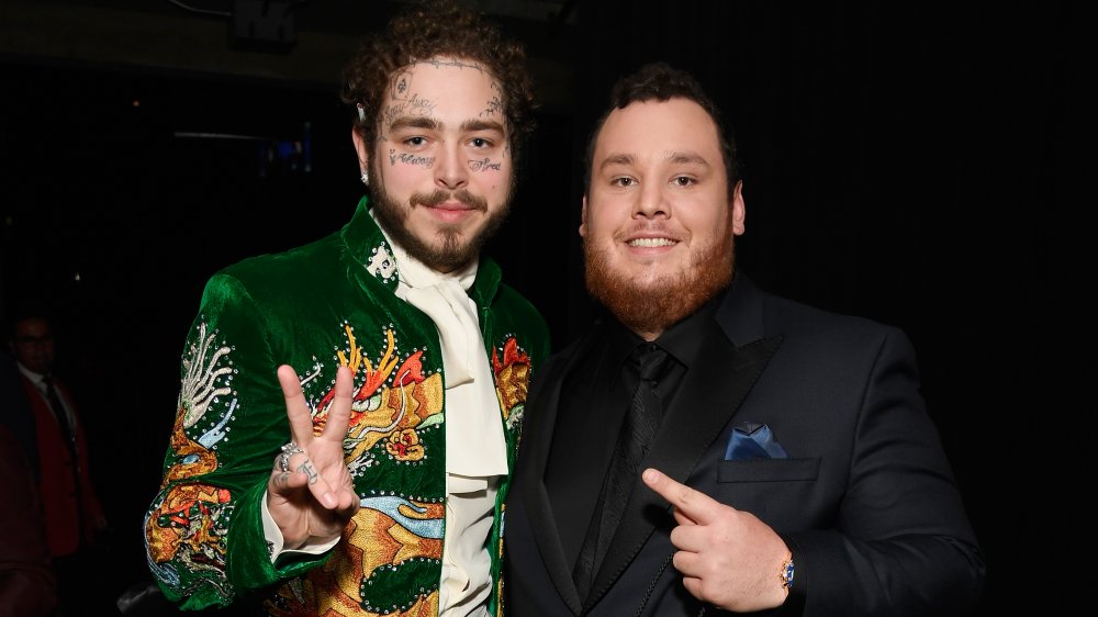 Post Malone in a green suit, Luke Combs in a black suit, posing together at an awards show