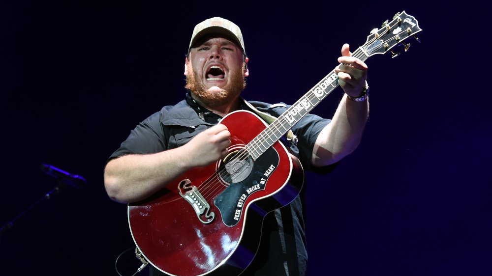 Luke Combs wearing black and playing a red guitar while singing on stage