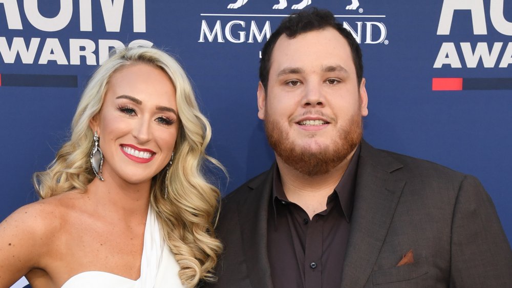 Nicole Hockings in a white dress, Luke Combs in a black suit, both smiling at an awards show