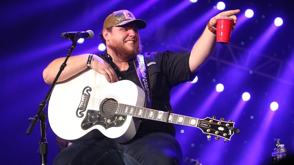 Luke Combs smiling on stage with a red solo cup