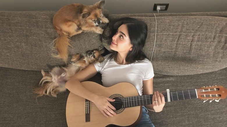 Melissa Barrera playing guitar, cuddling with her dogs