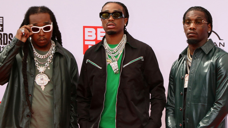 Migos, posing at an event, all wearing black jackets