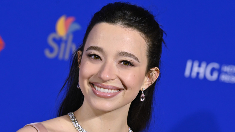 Mikey Madison smiling in front of a blue background