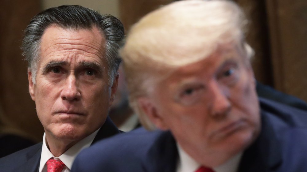 Mitt Romney looking stern seated behind Donald Trump