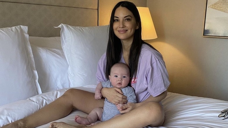 Olivia Munn, holding baby Malcolm on bed