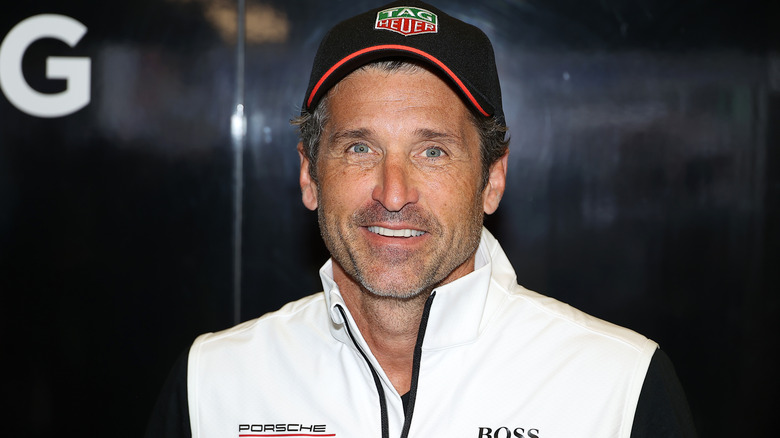 Patrick Dempsey posing in a hat and Porsche vest