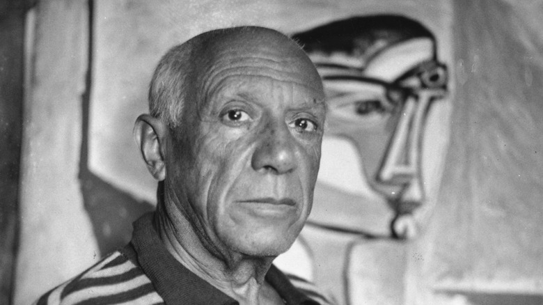 Pablo Picasso looks at camera with painting in background