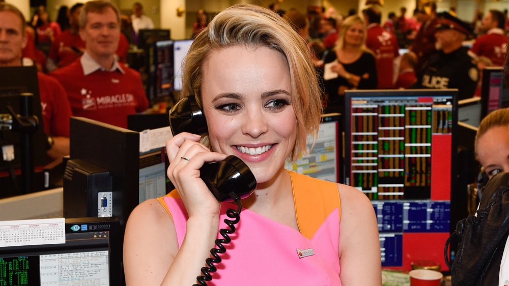 Rachel McAdams in an orange-and-pink dress, smiling while speaking on a telephone