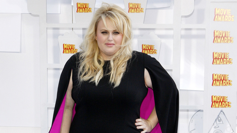 Rebel Wilson posing in a black dress on a red carpet