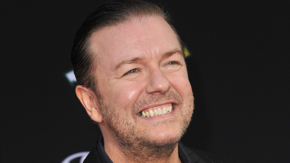 Ricky Gervais sporting a wincing smile 