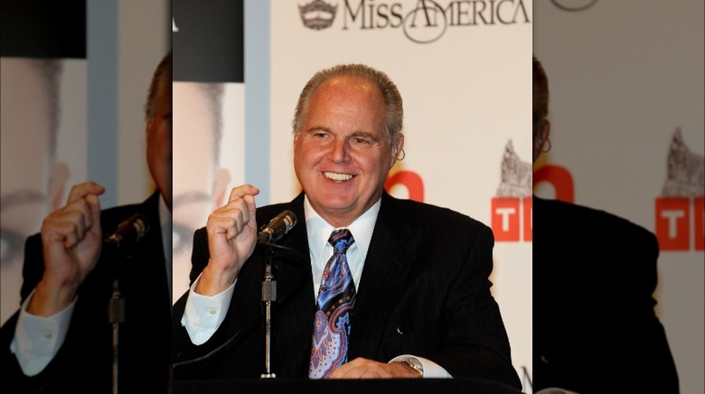 Rush Limbaugh smiling while seated at panel