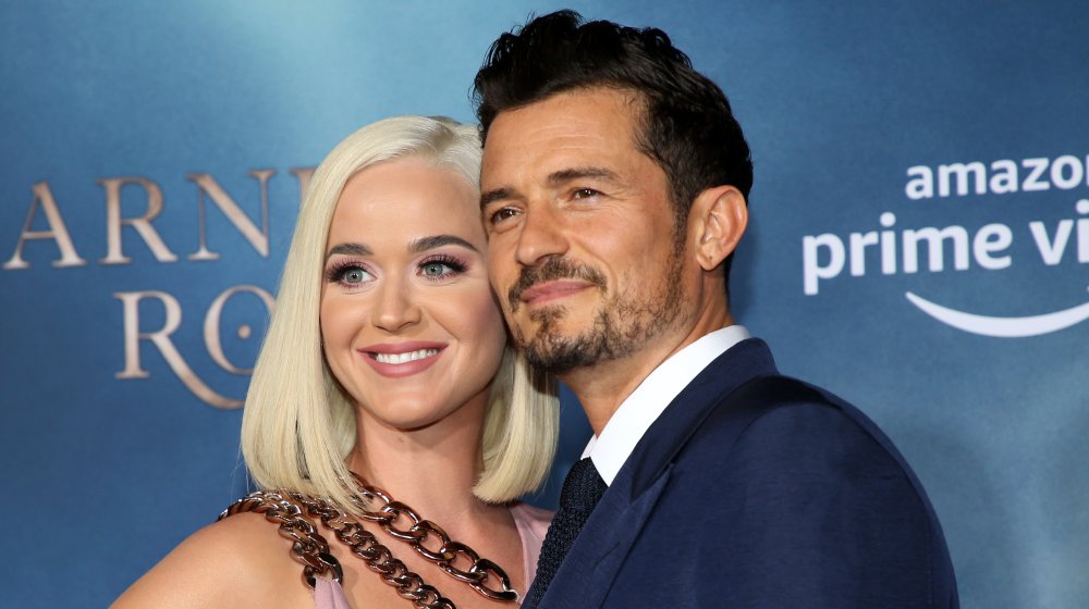 Katy Perry in a light pink dress and blonde hair, Orlando Bloom in a blue suit, both smiling at a premiere