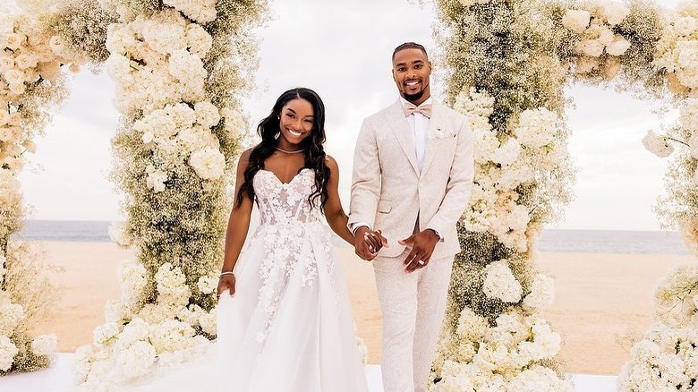 Simone Biles in a lacey white wedding dress and Jonathan Owens in a tan and white suit