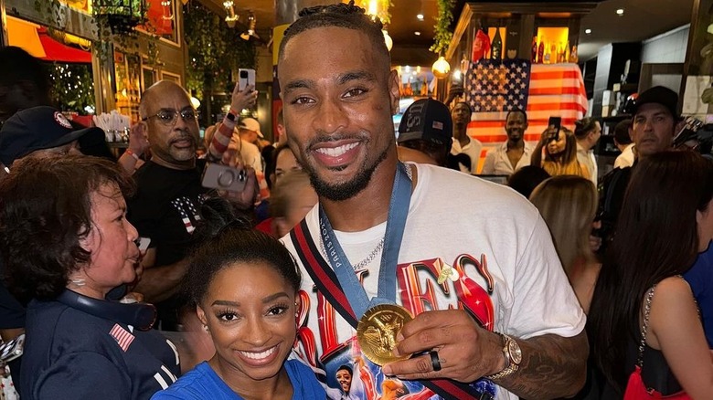 Simone Biles and Jonathan Owens wearing a white t-shirt and a gold Olympic medal