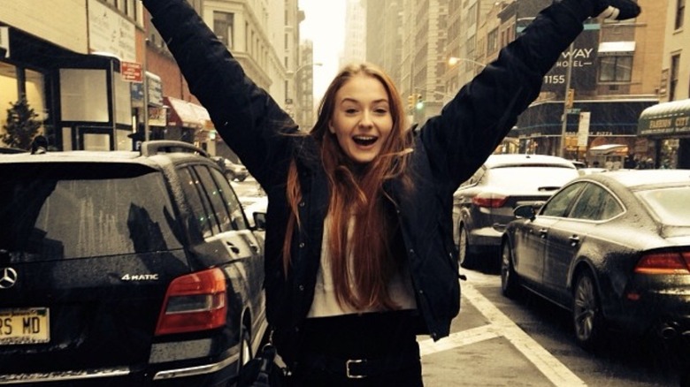 Sophie Turning standing in a city with her hands up