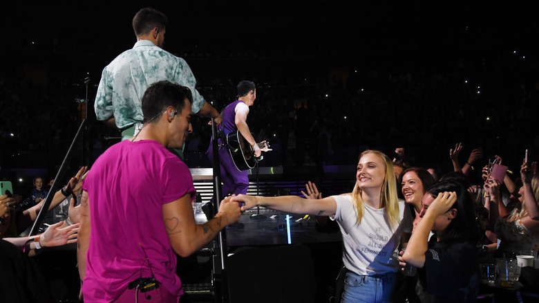 Sophie Turner reaching her hand out to Joe Jonas on stage