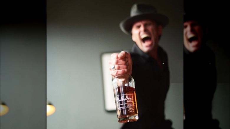 Walton Goggins displaying a bottle of his whiskey