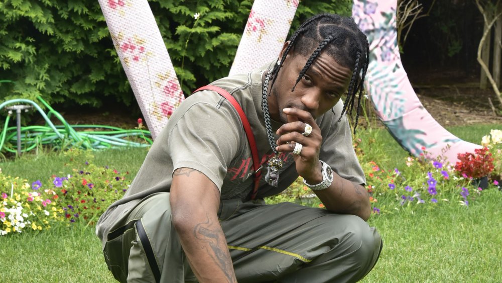 Travis Scott squatting with a hand over his mouth