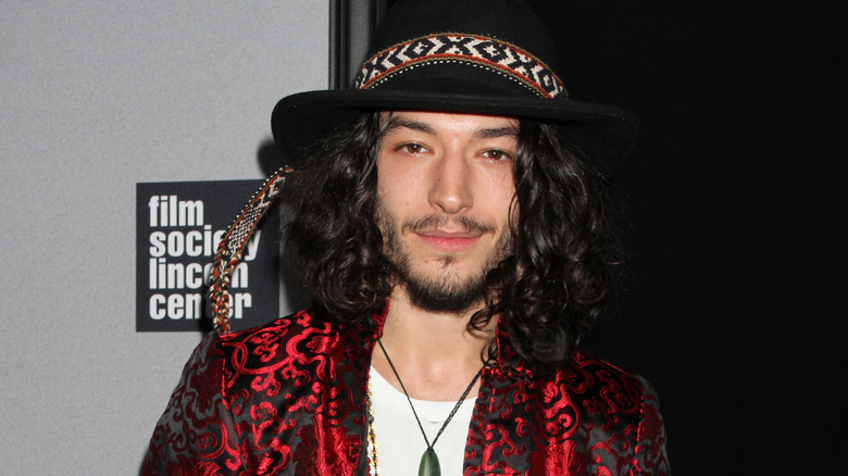 Ezra Miller dark hat red jacket posing