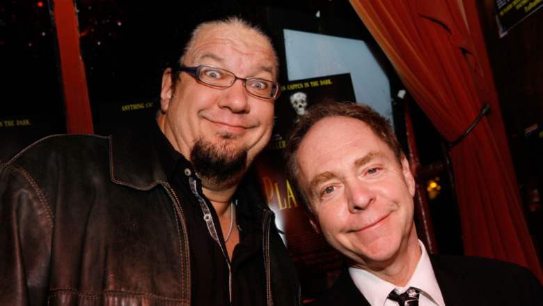 Magicians Penn and Teller smiling and leaning into one another 