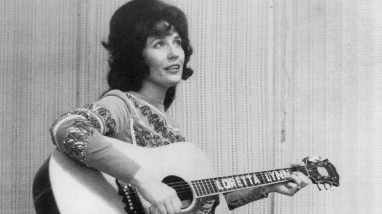 Loretta Lynn plays her guitar with thoughtful expression, 1965