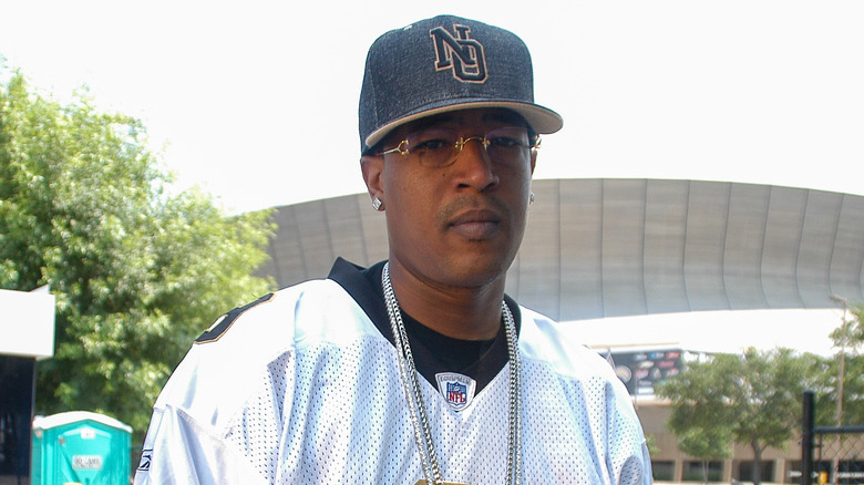 Corey 'C-Murder' Miller standing while wearing a cap, jersey, and chains