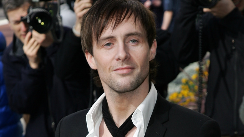 Ian Watkins smiling and posing for photographers while wearing a suit and tie