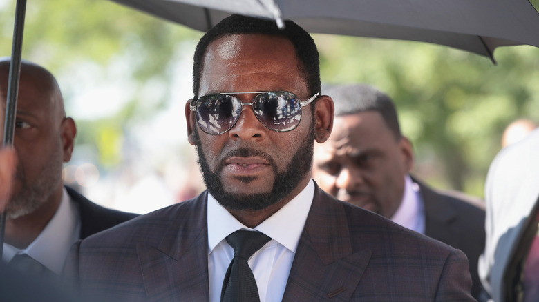 R. Kelly leaving a courthouse while wearing a suit under an umbrella