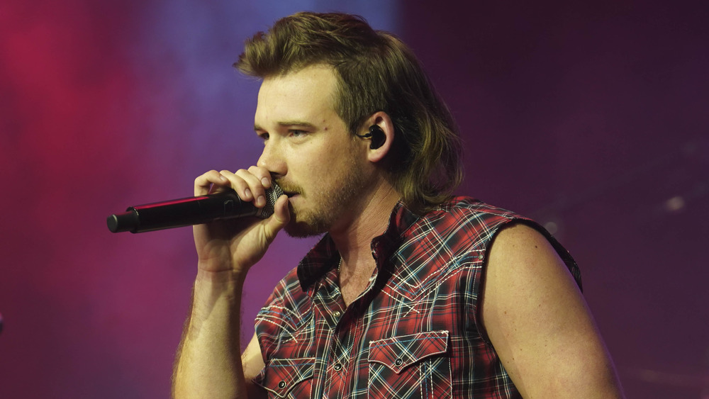 Morgan Wallen holds a microphone while performing