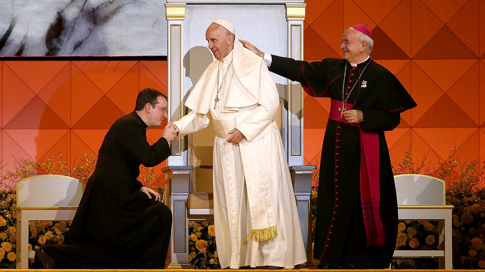 Priest kissing Pope Francis' ring as cardinal touches his shoulder